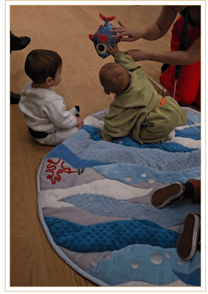 Deux bébés participent à un atelier d'éveil au musée, jouant sur un tapis sensoriel avec des objets colorés pour stimuler leurs sens.