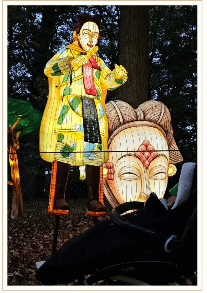 Grande sculpture lumineuse colorée représentant un personnage et un masque géant dans la forêt du parc de Thoiry, lors du festival des Lumières Sauvages.