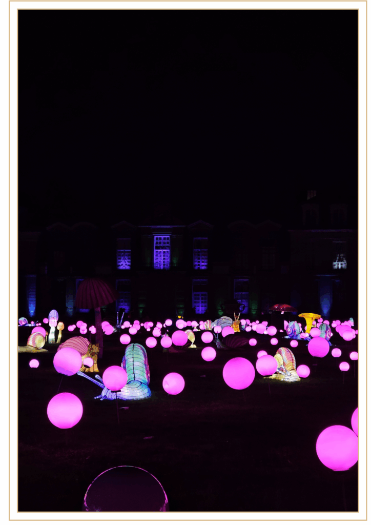 Installation lumineuse nocturne avec de nombreux escargots géants colorés et des sphères roses brillantes devant un bâtiment éclairé.