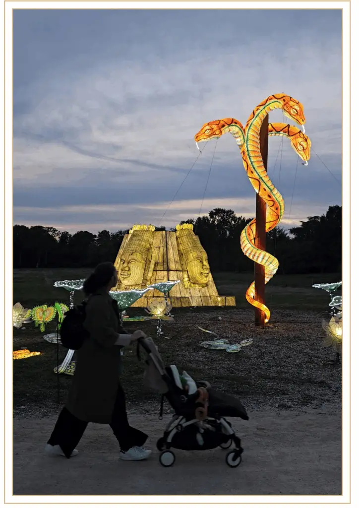 Parent avec poussette devant une sculpture lumineuse représentant un serpent géant et une pyramide dorée au festival des Lumières Sauvages de Thoiry.